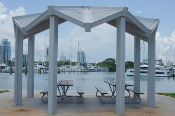 Modern Gazebo by Marina with Boats and Skyline in the Background. in St. Petersburg, FL. Open gazebo structure with picnic table overlooking marina with sailboats docked, skyscrapers, and waterfront. 