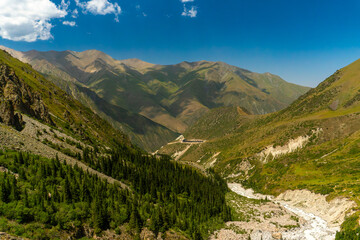 Naklejka premium Ala-Archa Mountain camp. Steep slopes, alpine meadows, coniferous forest, rocky riverbed. Distant summits ideal for hiking, mountaineering, backpacking, daytrips and wilderness adventure experiences