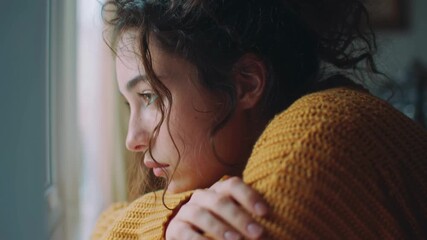 Close-up of a thoughtful young woman looking out the window in soft natural light, reflecting emotional struggles, family mental health, communication, and personal introspection at home.