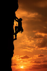 A rock climber silhouetted against a dramatic sunset, nearing the summit, symbolizing triumph and perseverance against nature.