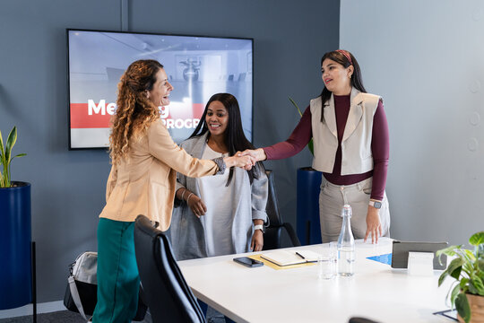 Female colleagues shaking hands across conference table in meeting room showing presentation slide