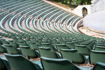 Fototapeta premium Large, open-air stone amphitheater is filled with numerous rows of green plastic seats arranged in a semi-circular pattern