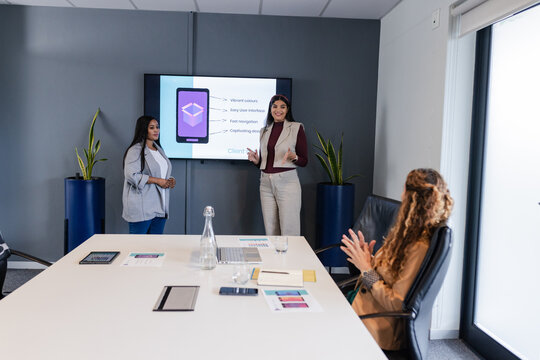 Professional women presenting mobile app on screen, applauding at conference table with laptop - Powered by Adobe