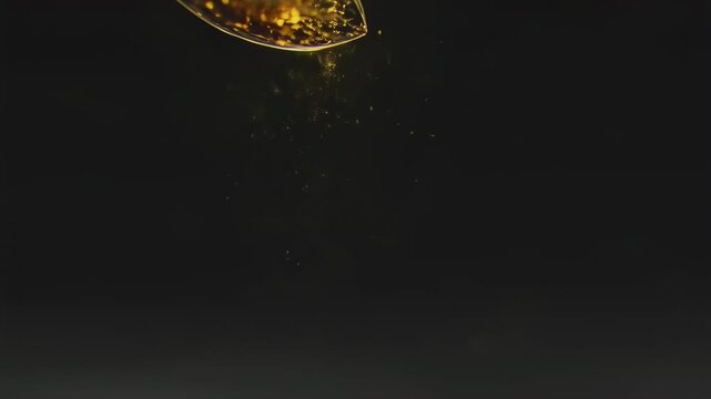 Closeup of a glowing amber-colored seed or pod falling through dark space with shimmering reflections and subtle motion effect
