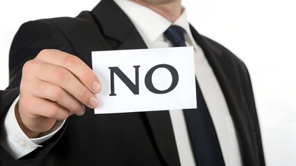 A person in a black suit holds a white card with “NO” in bold black letters near the camera, emphasizing rejection.