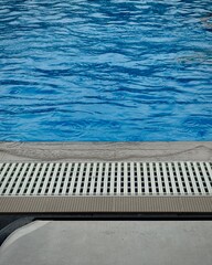 Blue swimming pool water with rain droplets and ripples near lounge chair on a cloudy day. 