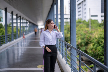 Fototapeta premium Businesswoman walking and talking on phone in modern city walkway