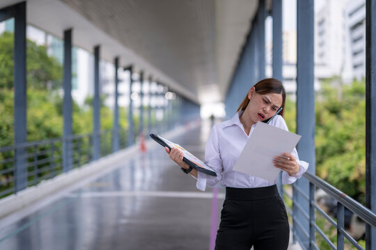 Stressed businesswoman talking on phone and reading documents in corridor