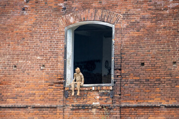 A mannequin sitting on a window of an abandoned red-brick factory