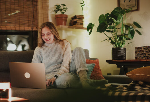 A young woman sitting comfortably on a couch using a laptop during a cozy and festive evening at home