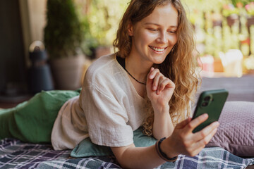 Beautiful young woman with a mobile phone in her hands lying on the summer terrace of a country house