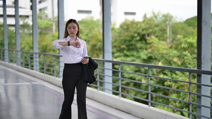 Businesswoman walking and checking time on smartwatch - Powered by Adobe