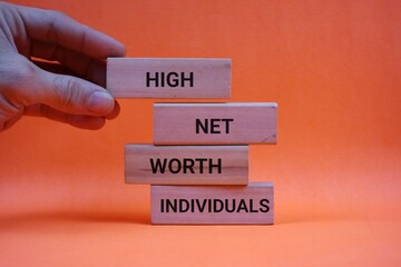 Hand holding a wooden block with the words "high, net, worth, individuals" written on it. Investment and finance concept. Isolated on an orange background.