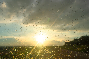 Raindrops on glass with golden sunset light through clouds, capturing peaceful and hopeful nature atmosphere