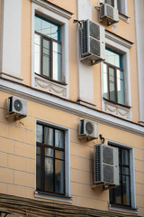 Facade of building with many air conditioners on windows in southern hot country. Yellow house exterior on city street. Escape from heat, creating favorable microclimate in urban apartments concept.