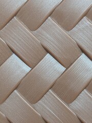 A flat weave pattern, resembling alternating strips stacked crisscrossing each other. A soft light brown or copper color, with a semi-glossy surface, resembling a brushed texture. It resembles a synth