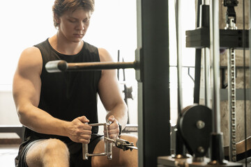 Young sporty caucasian man wearing blank sleeveless tank top exercising on low rowing machine at...