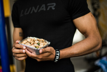 Muscular men holding healthy fitness meals in foil containers. Post-workout food, gym lifestyle, protein-rich takeaway lunch, athlete nutrition and meal prep for bodybuilding and recovery.