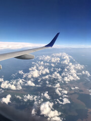 Obraz premium Airplane wing flying above clouds with blue sky view from window