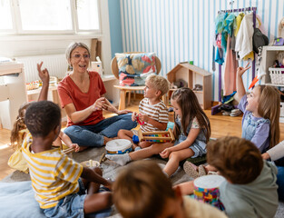 Preschool teacher leading a fun interactive activity with children sitting in a circle, raising hands and smiling in a bright classroom