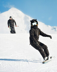 Close up front view woman black outfit snowboard downhill freeze motion. Active winter holidays, skiing downhill in sunny day. Bright image couple man woman skiers fast ski on steep hill downhill