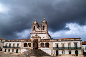 Obraz premium Nazaré, Oeste and Vale do Tejo, Portugal; March 11, 2018: The historic Sanctuary of Our Lady of Nazaré under a dramatic, stormy sky, showcasing its majestic facade and twin towers in Portugal