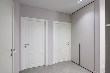 Modern hallway with two white paneled doors, a built-in wardrobe, and gray tile flooring. The walls are light lavender