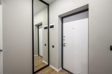 hallway with a full-length mirror and a white door with black trim. The walls are light gray, and the floor is a wood-like tile