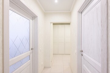 well-lit hallway with white doors, light-colored walls, and tiled floors. A closet can be seen at the end of the hallway