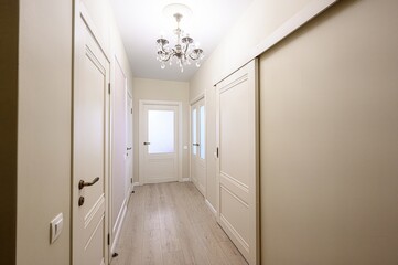 well-lit hallway with white doors and light wood flooring, illuminated by a decorative chandelier