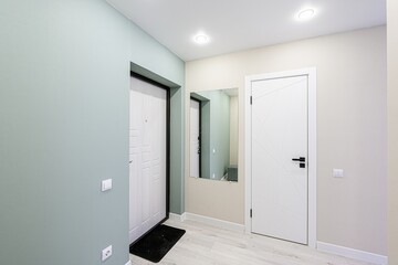 modern hallway featuring two white doors, a mirror, and pale walls. The color palette is light and airy, with minimalist design elements