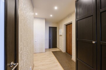 Hallway with patterned wallpaper, wood-look floor, and several doors. Dark wood wardrobe on the right. Recessed lighting