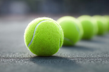 Close-up of bright yellow tennis balls arranged in a neat row on a textured gray surface, perfect for sports, recreation, or competition themes.