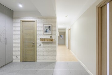 bright hallway with light wood doors, white brick accent wall, and gray tile floor. The space is minimalist with clean lines