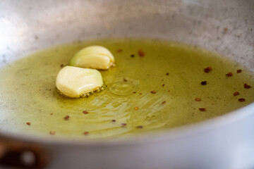 Garlic cloves sizzling in olive oil with chili flakes in a pan. A classic home cooking step to infuse oil with flavor, often used as the base for Italian and Mediterranean dishes