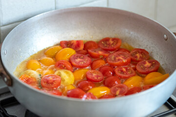Fresh colorful mix of red and yellow cherry tomatoes cooking in a pan with olive oil on the stove in a kitchen