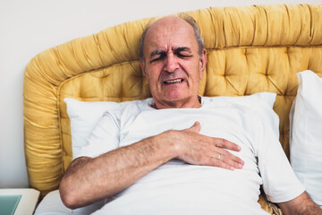 Elderly man feeling pain in chest after waking up in the morning and lying in bed. He is worried and possibly experiencing early signs of heart attack.	