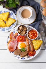 Full Irish or English breakfast with sausages, bacon, pudding, fried egg with runny yolk, hash browns, beans and tomatoes. View from above, top studio shot