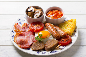 Full Irish or English breakfast with sausages, bacon, pudding, fried egg with runny yolk, hash browns, beans and tomatoes