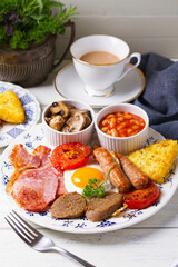 Full Irish or English breakfast with sausages, bacon, pudding, fried egg with runny yolk, hash browns, beans and tomatoes