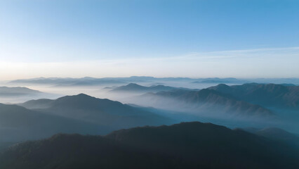 Fototapeta premium Aerial view of layered mountain ranges at dawn with soft blue sky and morning mist.