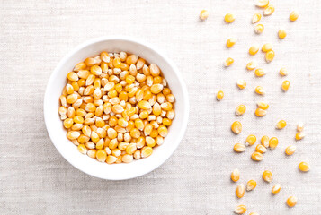 Popcorn kernels, in a white bowl on linen. Seeds of Zea mays variety everta, rounded at the top, which expand and puffs up, when heated. Snack food, sometimes sold as pearls, or as old maids.