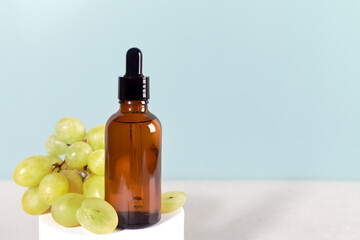 Grape seed oil in dropper bottle with green grapes. Skin care aromatherapy on blue background