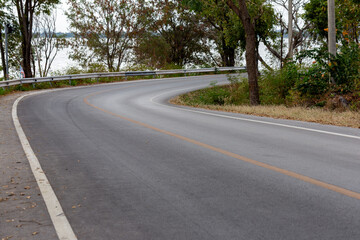 An empty, winding asphalt road curves through a green summer forest, a journey into nature's quiet landscape