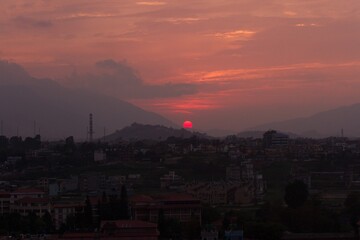 Himalayan Glow: Red Sun Setting in Nepal&rsquo;s Hills
