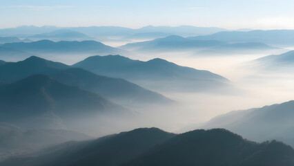 Aerial view of layered mountain ranges at dawn with soft blue sky and morning mist.