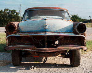Front of a very rusty 1950's car with parts removed in a small town in Texas