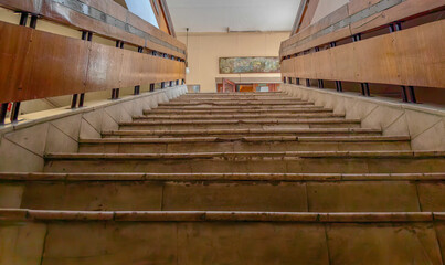 An upward perspective captures an old staircase with wooden handrails and a painting.
