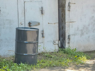Obraz premium A weathered gray metal barrel rests in front of a garage door