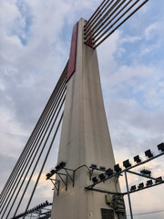 Dramatic upward view of a modern concrete bridge pylon with steel cables against a twilight sky. Bandung Iconic Bridge.